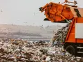 Pomarańczowa śmieciarka wysypuje odpady na wysypisku. Wokół latają mewy. Zastanawiasz się, gdzie oddać plastiki samochodowe? To miejsce nie jest odpowiednie.