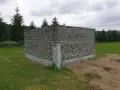 Nietypowy domek z butelek plastikowych, zbudowany z tysięcy szklanych opakowań, otoczony zielenią i drzewami.