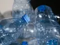 Stos pustych, przezroczystych butelek PET z niebieskimi nakrętkami, gotowych do recyklingu.