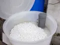 Duży biały pojemnik wypełniony tabletkami soli do zmiękczacza wody. W środku widoczny szary element instalacji.