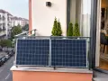 Dwa panele fotowoltaiczne na tarasie, z widokiem na ulicę i kamienice. Zielone tuje dodają uroku tej ekologicznej instalacji.