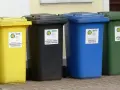 Cztery kolorowe pojemniki na śmieci: żółty, czarny, niebieski i zielony. Każdy przeznaczony do segregacji odpadów, pokazując, ile pojemników na śmieci na osobę jest potrzebne.
