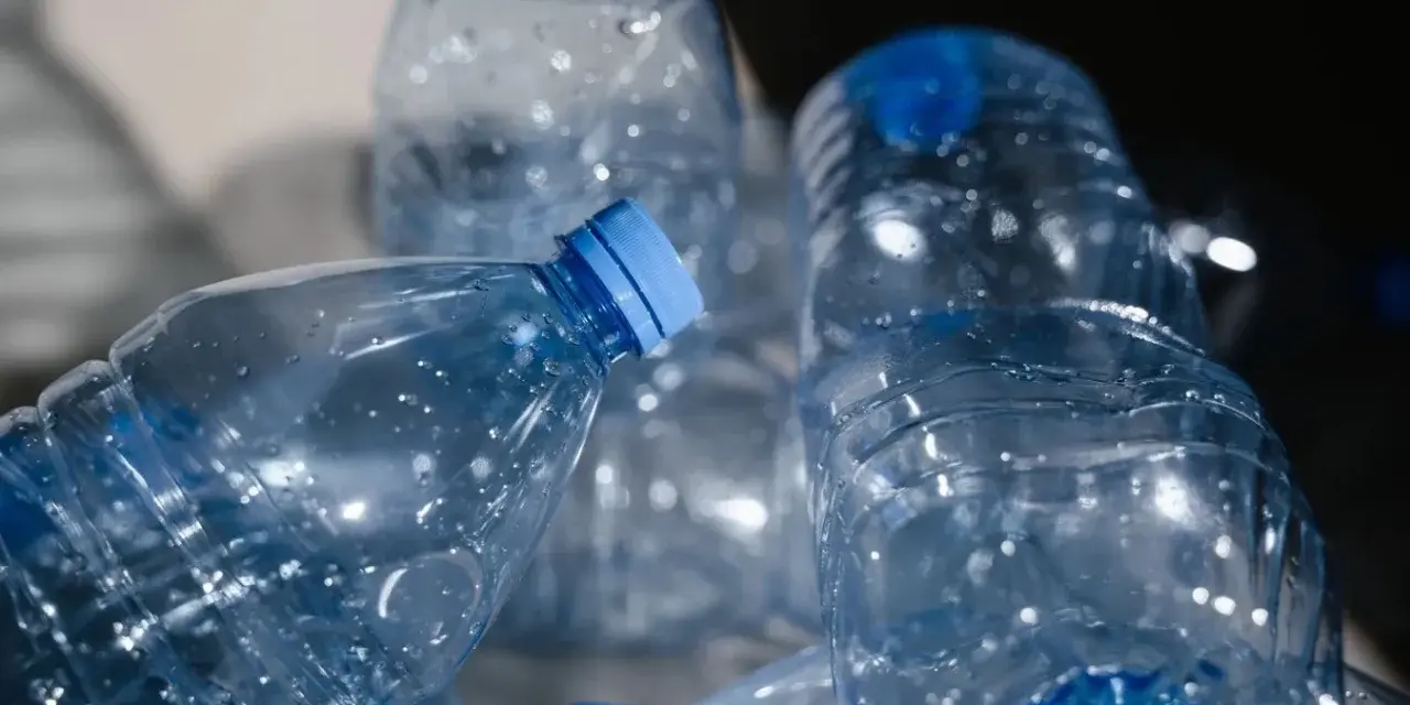 Stos pustych, przezroczystych butelek PET z niebieskimi nakrętkami, gotowych do recyklingu.
