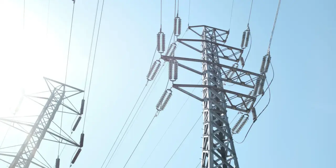 Wysokie słupy energetyczne z przewodami, przypominające o potrzebie oszczędzania i rozsądnym zarządzaniu abonamentem za prąd.
