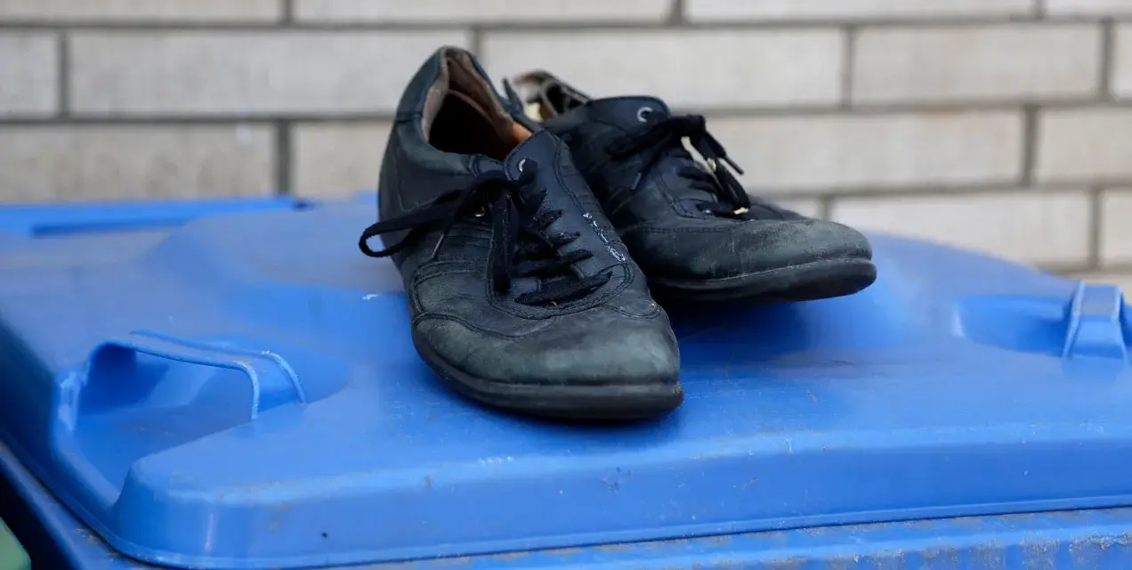 Stare, czarne buty leżą na niebieskim koszu na śmieci. Czas pomyśleć, gdzie wyrzucić buty, gdy już się zużyją.