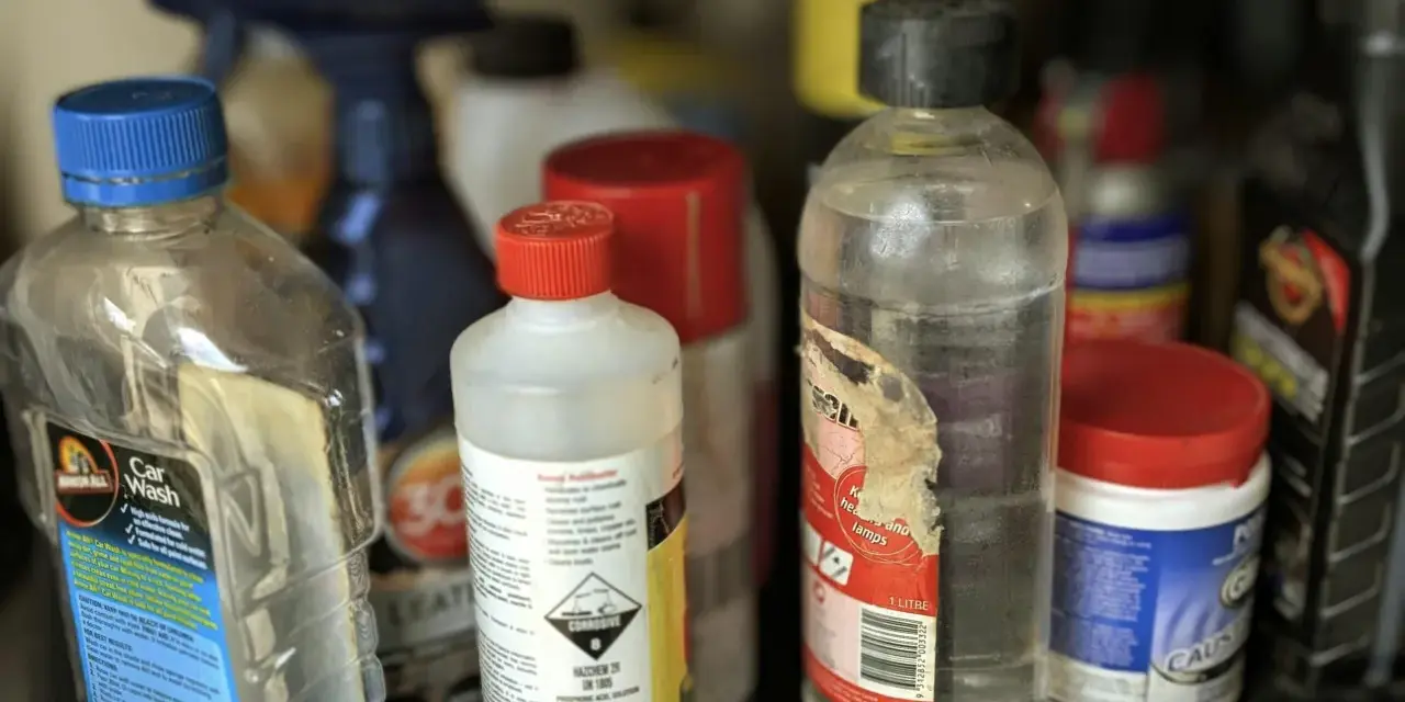 Na półce stoją różne butelki z płynami. Jedna z nich, z etykietą "Car Wash", sugeruje, gdzie wylać rozpuszczalnik, jeśli jest to konieczne.