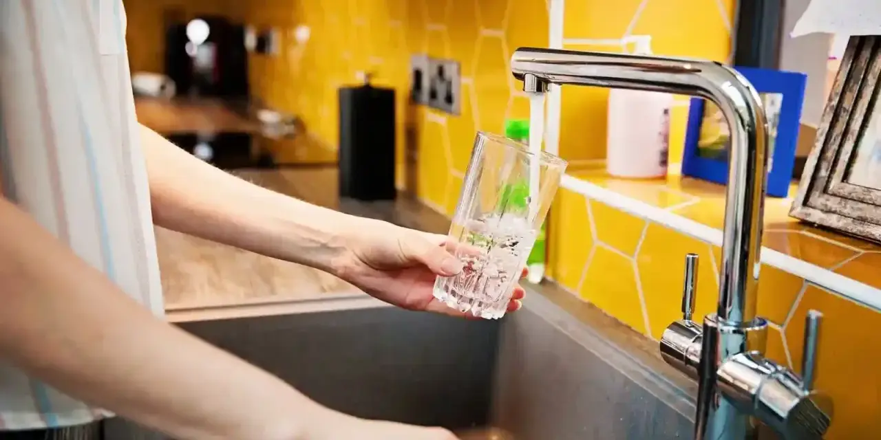 Ręka nalewa wodę do szklanki z kranu. To jak małe złoże do stacji uzdatniania wody w domu, zapewniające czystość.