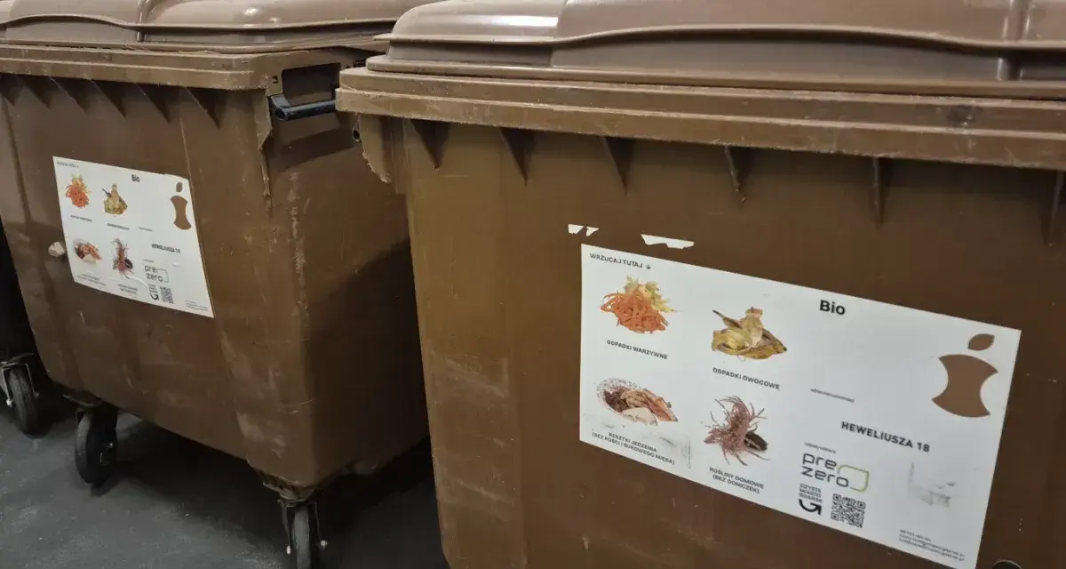 Brązowe kontenery na odpady bio. Naklejka informuje, co można wyrzucać, sugerując, że odpady bio można wyrzucać w workach.