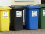 Cztery kolorowe pojemniki na śmieci: żółty, czarny, niebieski i zielony. Każdy przeznaczony do segregacji odpadów, pokazując, ile pojemników na śmieci na osobę jest potrzebne.