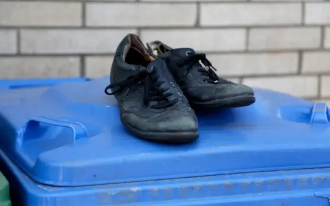 Stare, czarne buty leżą na niebieskim koszu na śmieci. Czas pomyśleć, gdzie wyrzucić buty, gdy już się zużyją.