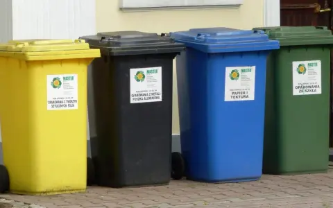 Cztery kolorowe pojemniki na śmieci: żółty, czarny, niebieski i zielony. Każdy przeznaczony do segregacji odpadów, pokazując, ile pojemników na śmieci na osobę jest potrzebne.