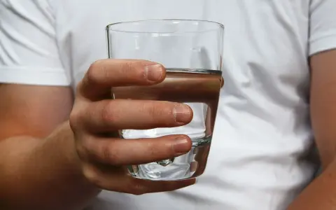 Dłoń trzyma szklankę z wodą. Czy twarda woda jest zdrowa? To pytanie nurtuje wielu.