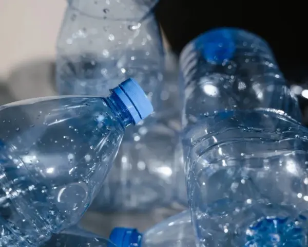 Stos pustych, przezroczystych butelek PET z niebieskimi nakrętkami, gotowych do recyklingu.