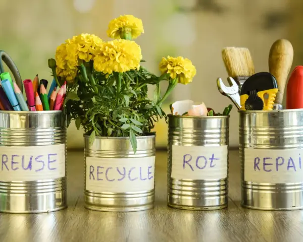 Cztery puszki po konserwach z napisami: REUSE, RECYCLE, ROT, REPAIR. W pierwszej nożyczki i kredki, w drugiej kwiaty, w trzeciej skorupki jajek, w czwartej narzędzia. Jak zrobić zgniatarkę do puszek?