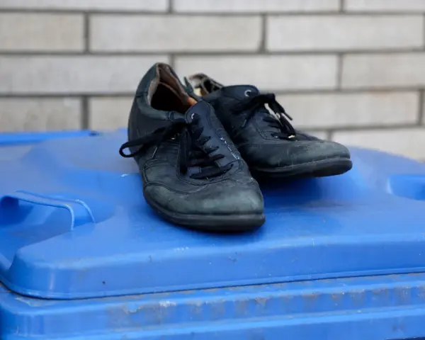 Stare, czarne buty leżą na niebieskim koszu na śmieci. Czas pomyśleć, gdzie wyrzucić buty, gdy już się zużyją.