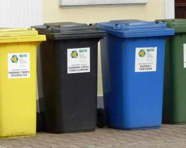 Cztery kolorowe pojemniki na śmieci: żółty, czarny, niebieski i zielony. Każdy przeznaczony do segregacji odpadów, pokazując, ile pojemników na śmieci na osobę jest potrzebne.