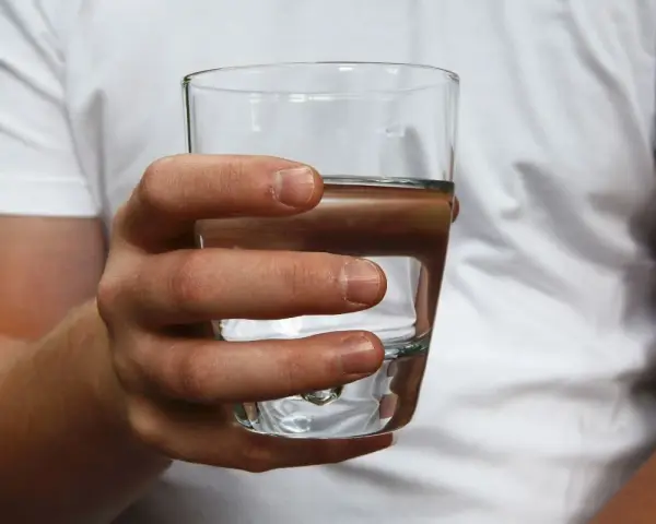 Dłoń trzyma szklankę z wodą. Czy twarda woda jest zdrowa? To pytanie nurtuje wielu.