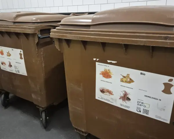 Brązowe kontenery na odpady bio. Naklejka informuje, co można wyrzucać, sugerując, że odpady bio można wyrzucać w workach.