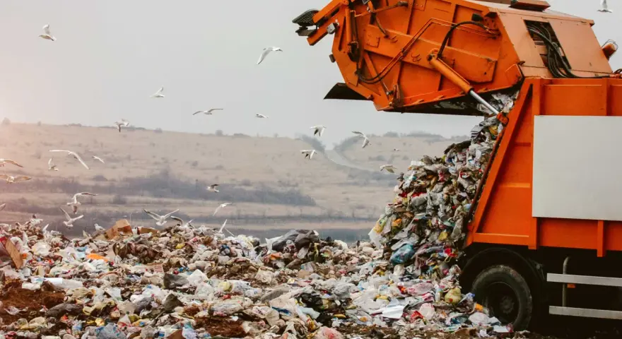 Pomarańczowa śmieciarka wysypuje odpady na wysypisku. Wokół latają mewy. Zastanawiasz się, gdzie oddać plastiki samochodowe? To miejsce nie jest odpowiednie.