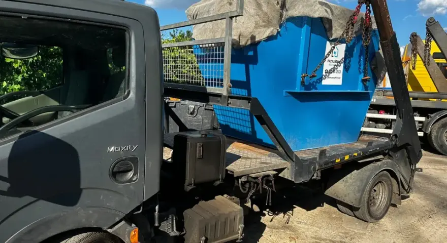 Niebieski kontener na śmieci, przykryty płachtą, jest ładowany na ciężarówkę. Czy PCV to plastik? Tak, to rodzaj plastiku.