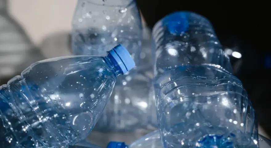 Stos pustych, przezroczystych butelek PET z niebieskimi nakrętkami, gotowych do recyklingu.