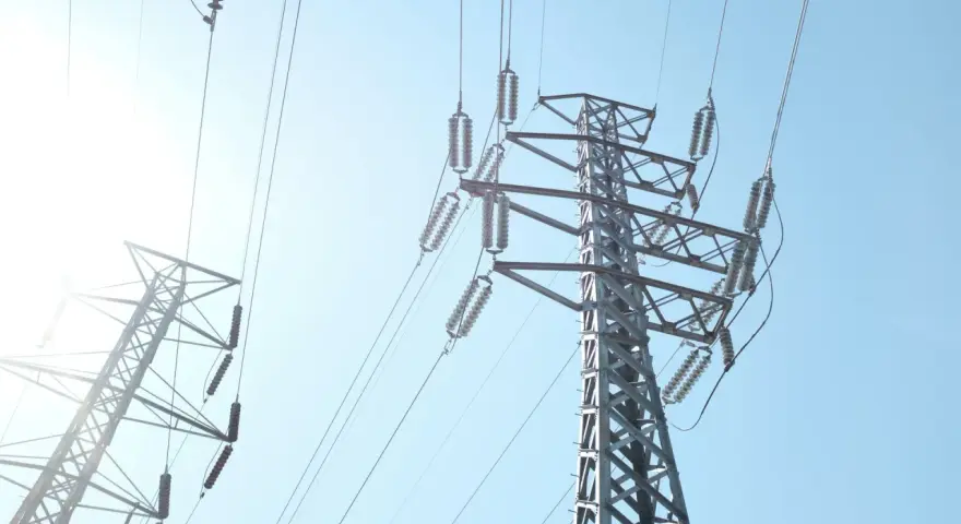 Wysokie słupy energetyczne z przewodami, przypominające o potrzebie oszczędzania i rozsądnym zarządzaniu abonamentem za prąd.