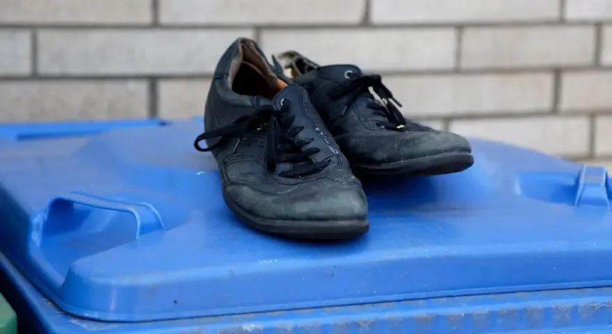 Stare, czarne buty leżą na niebieskim koszu na śmieci. Czas pomyśleć, gdzie wyrzucić buty, gdy już się zużyją.