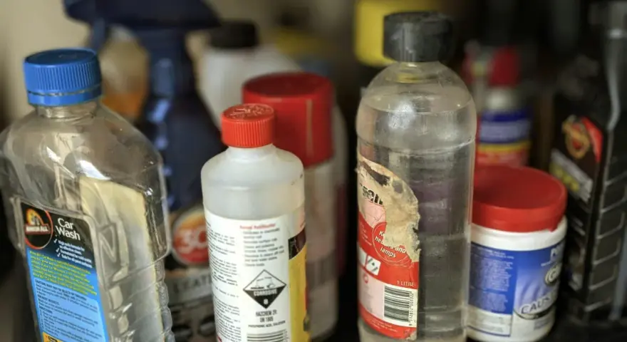 Na półce stoją różne butelki z płynami. Jedna z nich, z etykietą "Car Wash", sugeruje, gdzie wylać rozpuszczalnik, jeśli jest to konieczne.