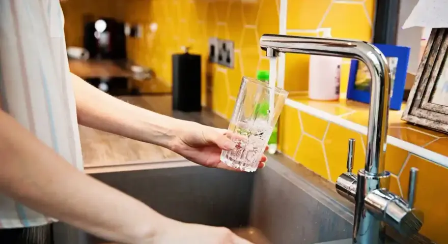 Ręka nalewa wodę do szklanki z kranu. To jak małe złoże do stacji uzdatniania wody w domu, zapewniające czystość.