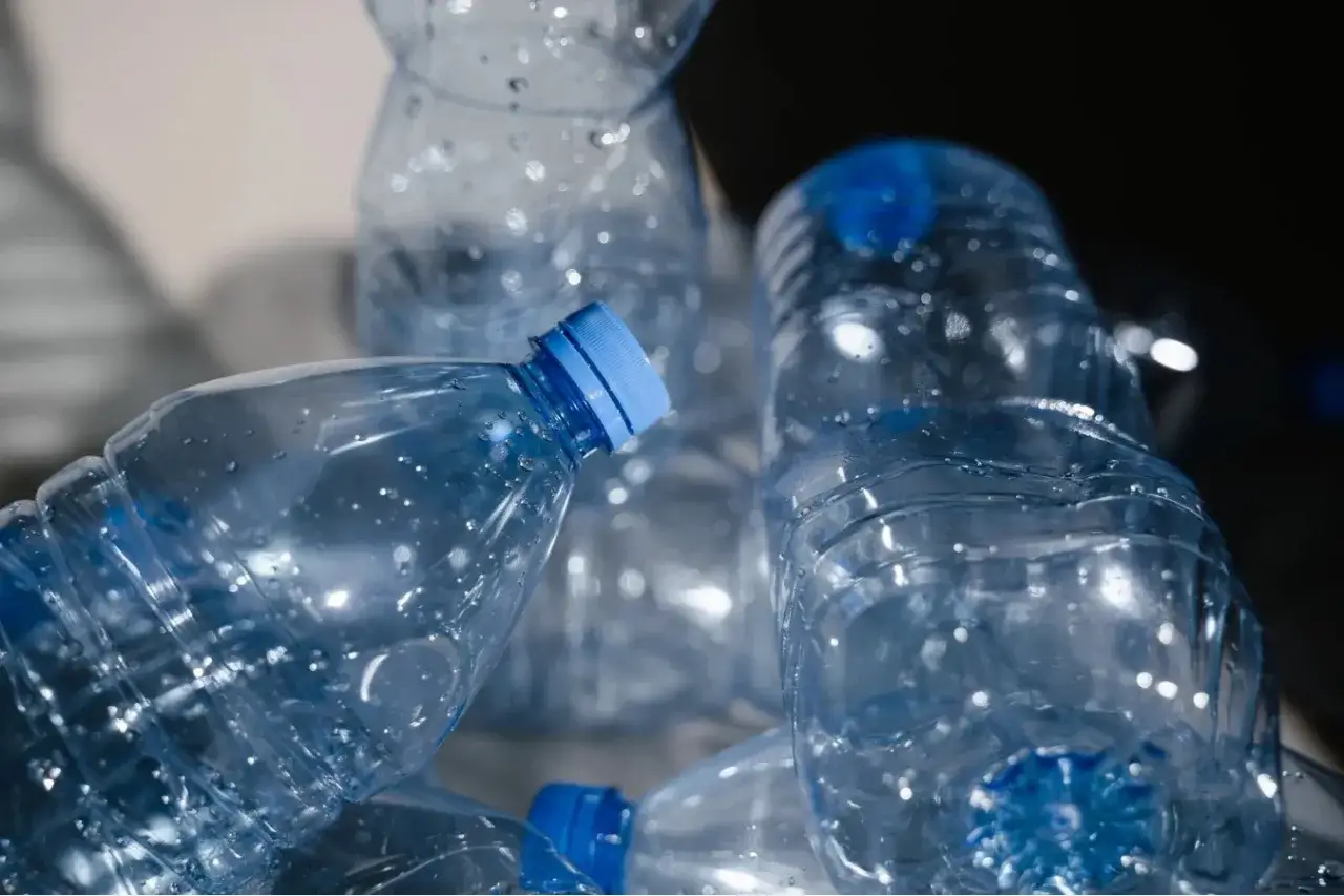Stos pustych butelek PET z niebieskimi nakrętkami, gotowych do recyklingu. Produkcja butelek PET to ważny etap w ich życiu.