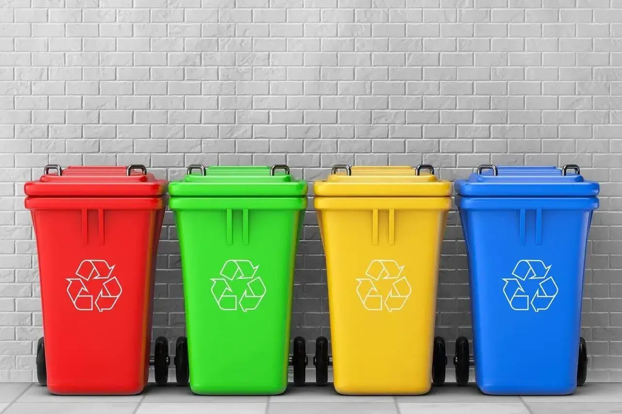 Cztery kolorowe kosze na śmieci (czerwony, zielony, ż&oacute;łty, niebieski) z symbolem recyklingu. To przykłady segregacji odpad&oacute;w komunalnych.