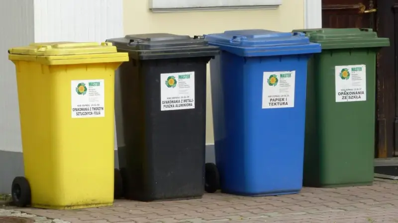 Cztery kolorowe pojemniki na śmieci: żółty, czarny, niebieski i zielony. Każdy przeznaczony do segregacji odpadów, pokazując, ile pojemników na śmieci na osobę jest potrzebne.